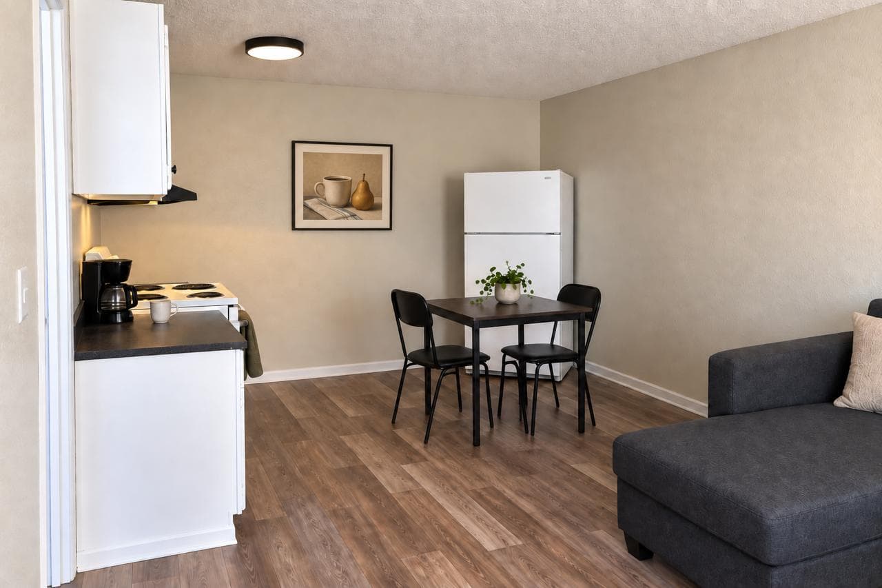 Cocina con estufa eléctrica, cafetera, refrigerador y mesa para dos